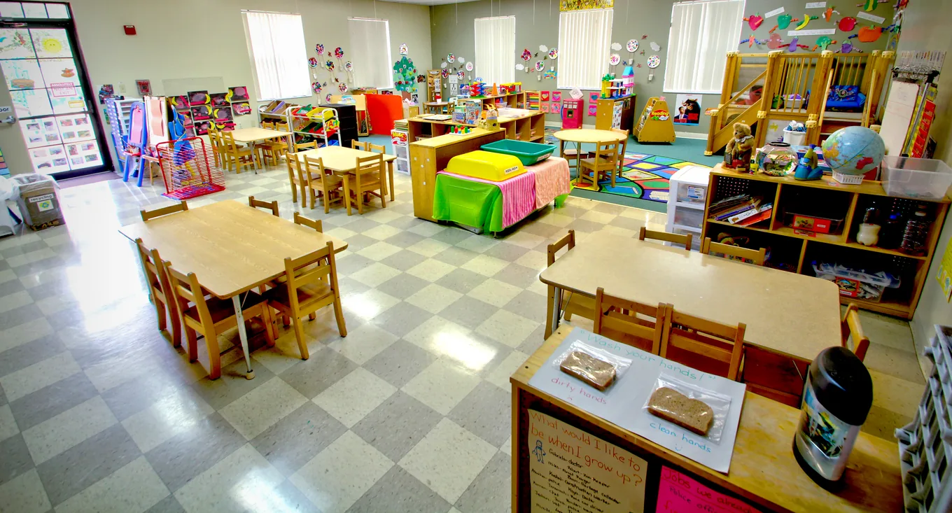 A classroom set up with tables and rolled nap mats