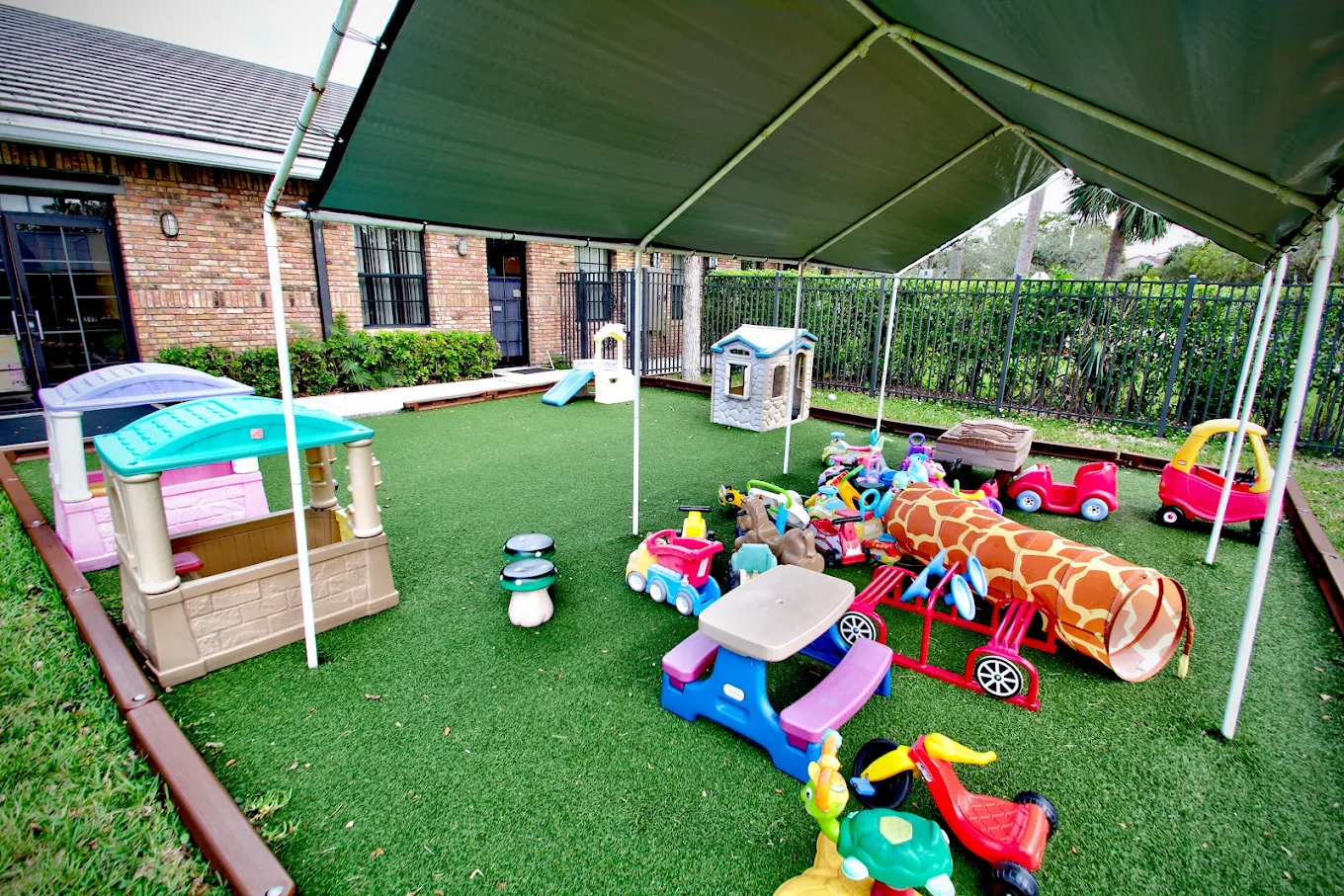 Covered outdoor play area with ride-on toys, playhouses, and a tunnel